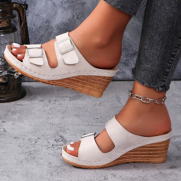 Creamy-white women's wedge slippers with a buckle strap on a black sole.