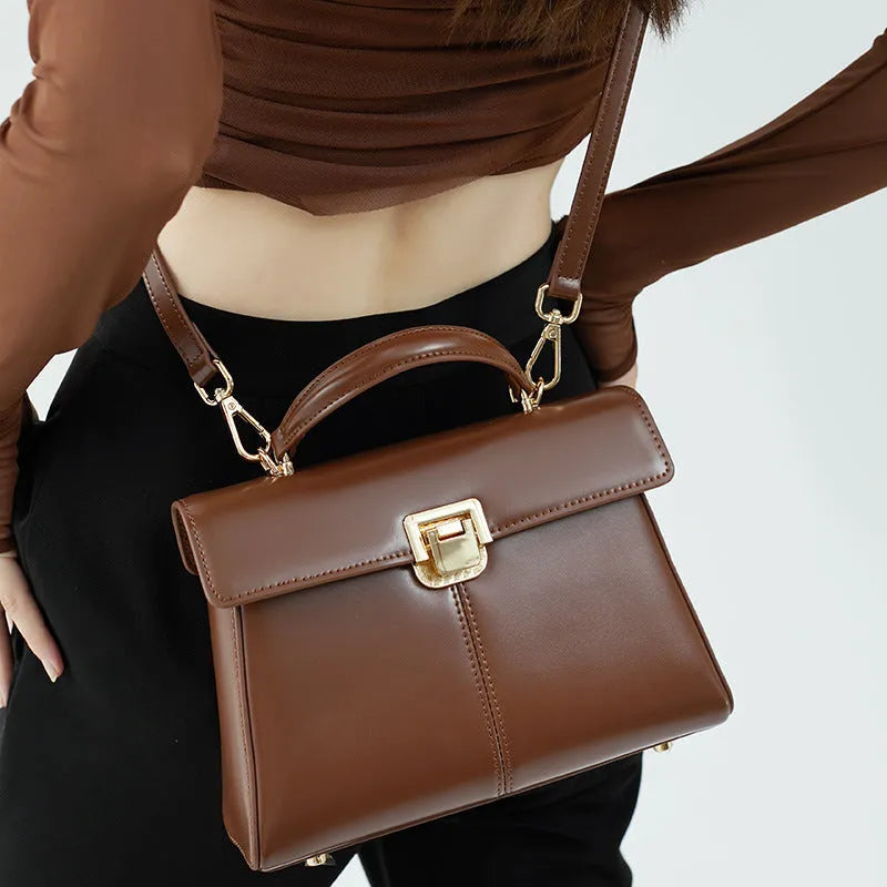 Women's black genuine leather shoulder bag with a clasp, shown with adjustable strap and open to reveal internal zippered pocket.