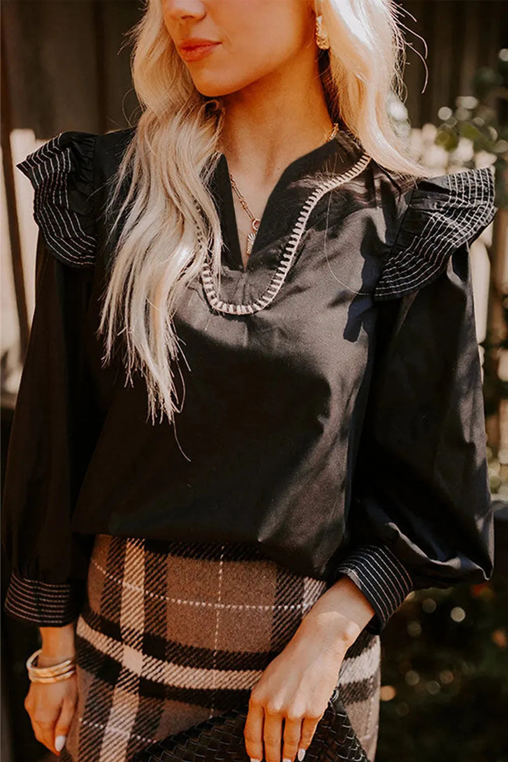 Black long sleeve women's blouse with V-neck, contrast stitching, and ruffle sleeve details.