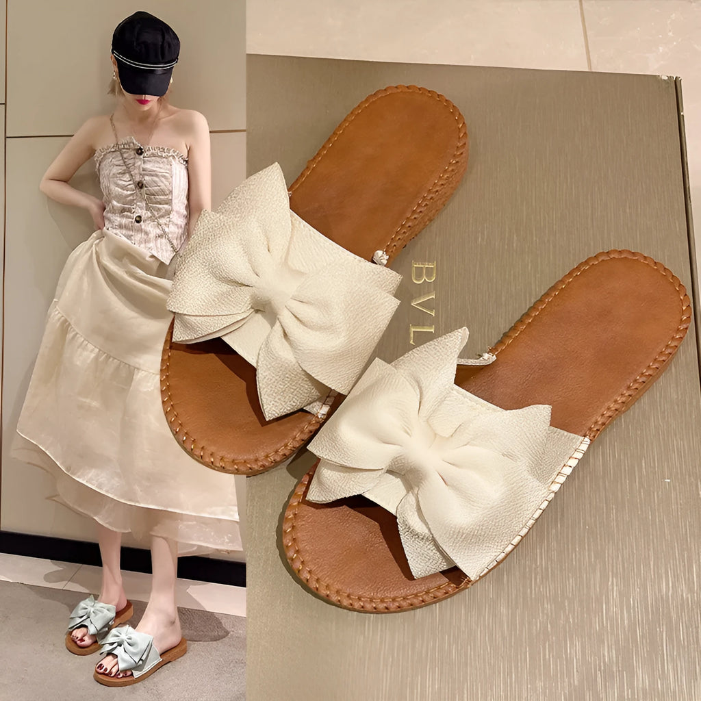 Women's beige suede slip-on sandals with a bow detail and soft rubber sole.