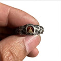 Close-up of a hand-forged copper ring with a rock texture and a carved Buddha design.
