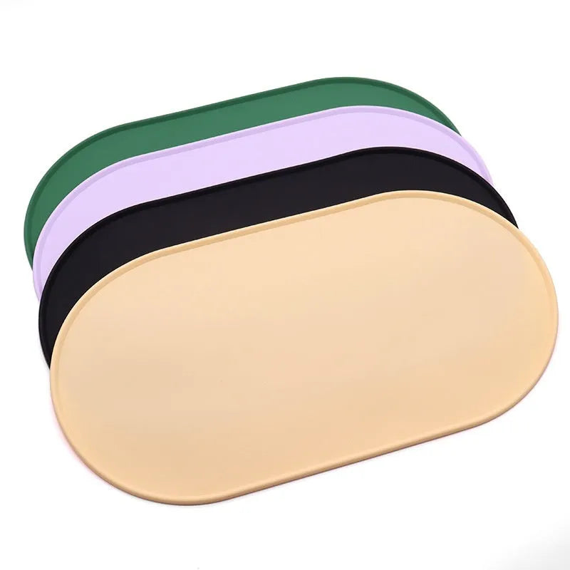 Beige silicone cat feeding mat with raised edge containing a food bowl and scattered kibble on a kitchen floor.