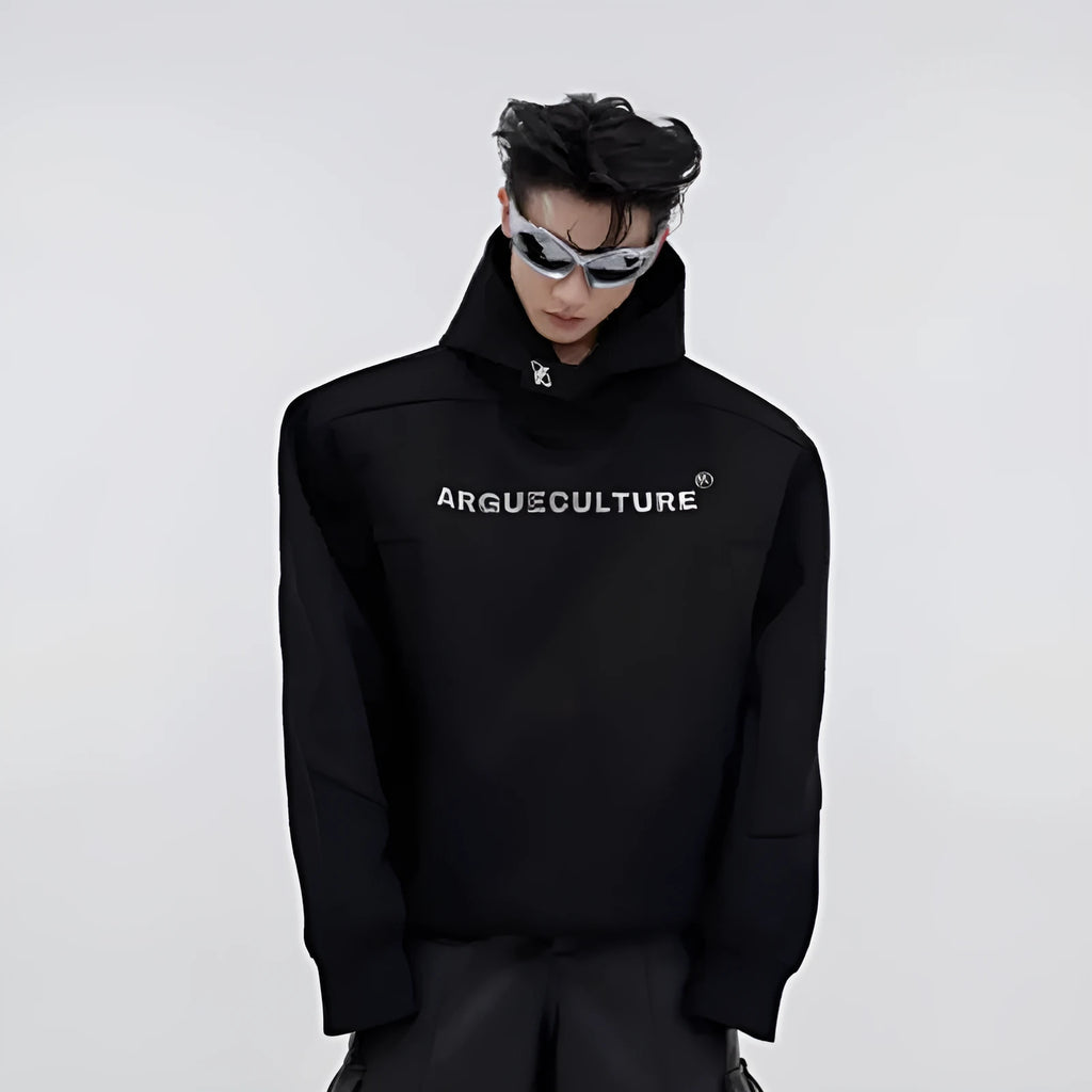 Man modelling a loose grey hooded sweater with heavy shoulder pads and raised metal-effect graphic printing on the front.