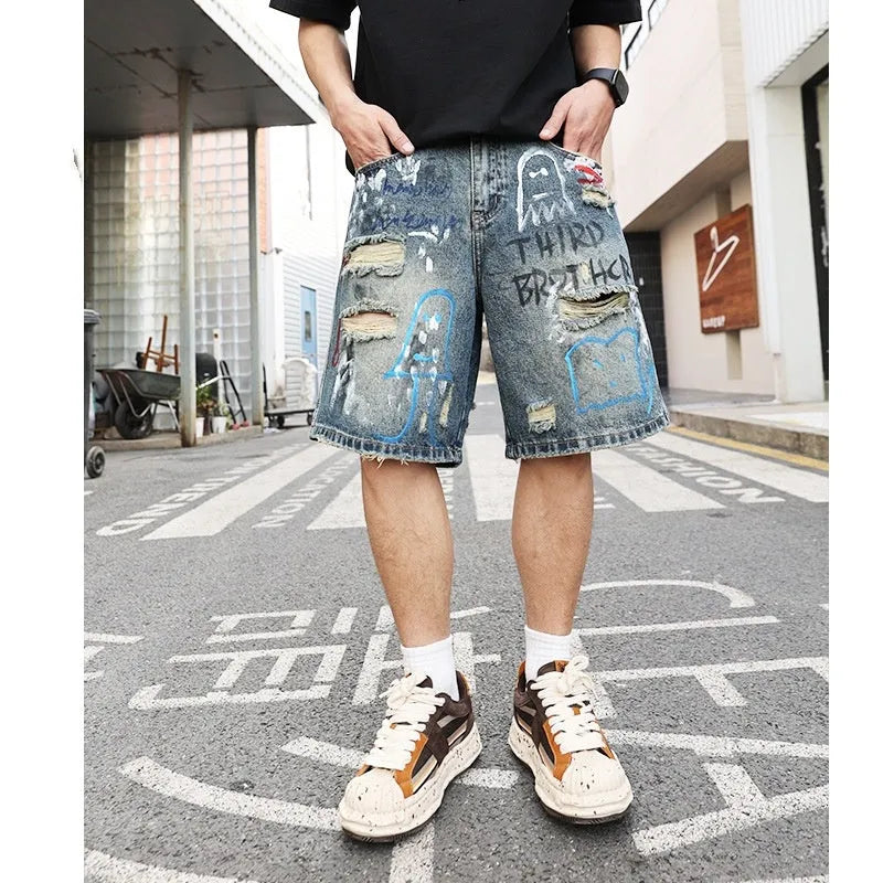 Blue men's ripped denim shorts with graffiti style and straight leg cut on a hanger.