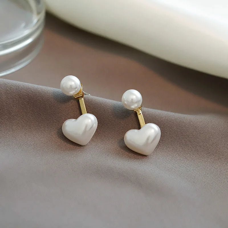 Close-up of women's heart-shaped alloy stud earrings with inlaid pearl-like artificial gems on a white background.