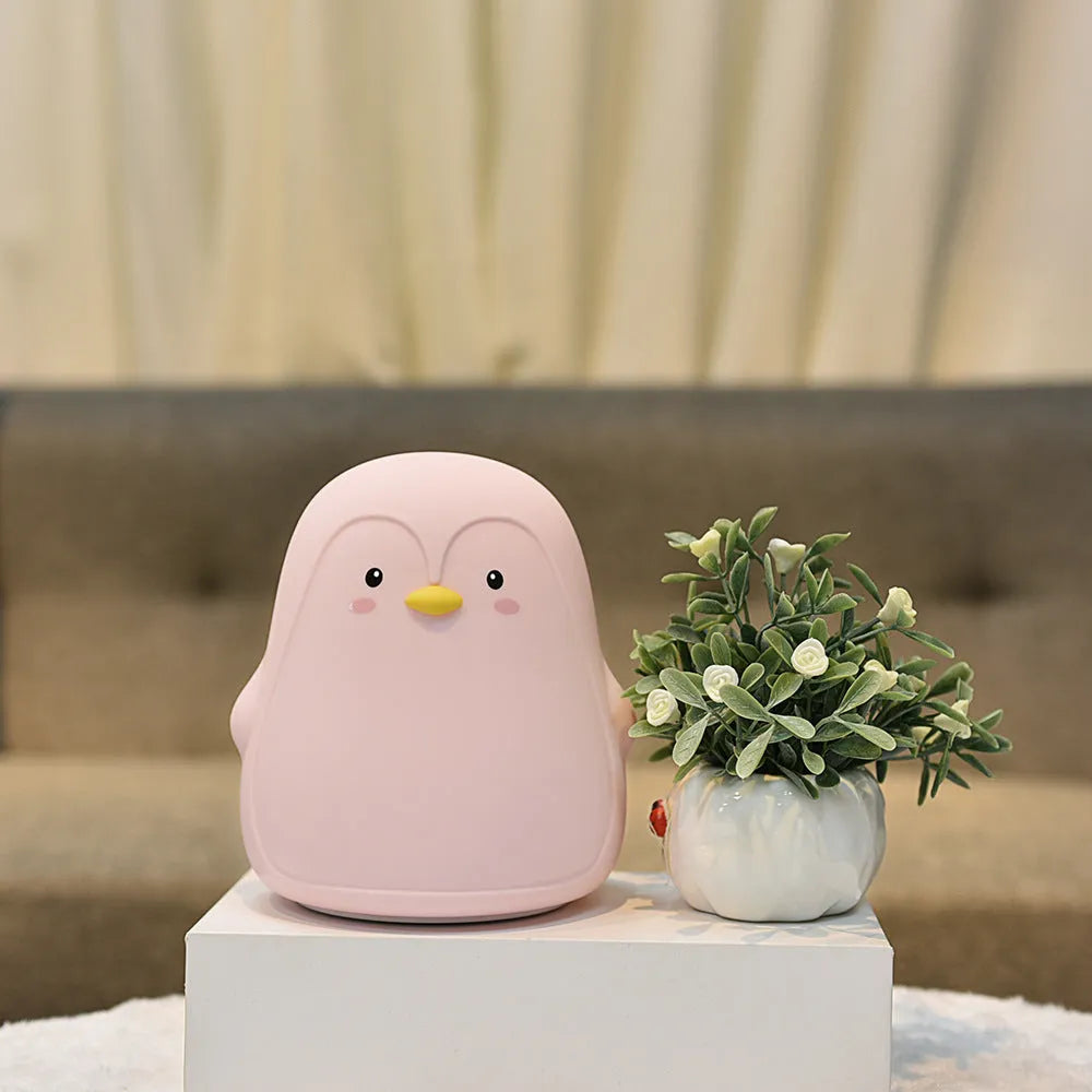 White USB rechargeable penguin-shaped night light with soft glow, shown next to its charging cable.