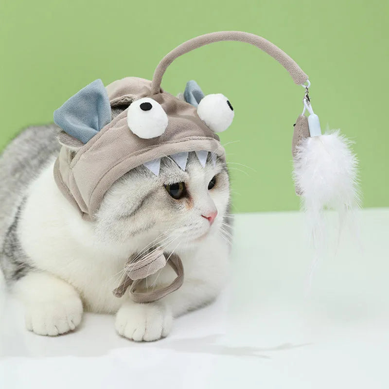 Grey dinosaur-themed cat headband toy with big eyes, a feather teaser, and an adjustable strap for hands-free play.