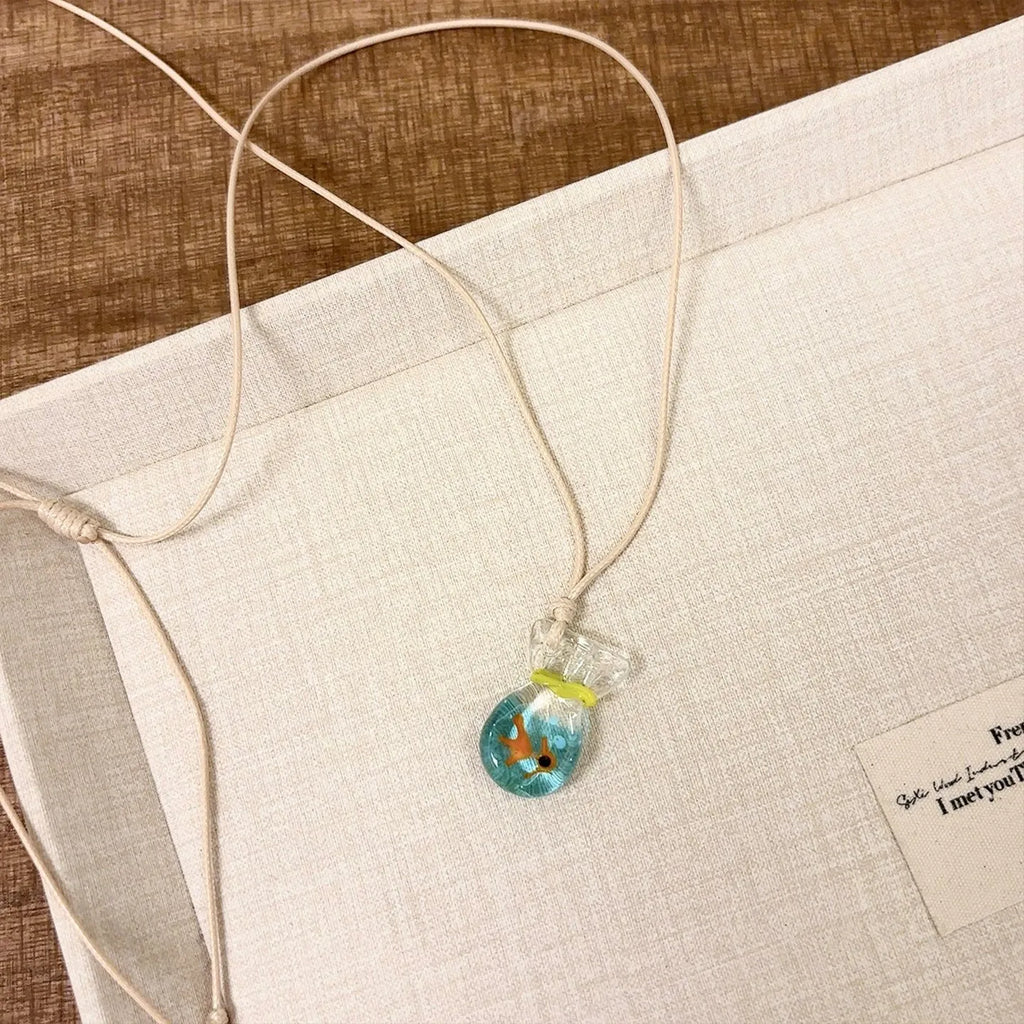 Women's necklace with a blue hand-painted fish charm on a beige cotton and linen clavicle chain.