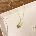 Women's necklace with a blue hand-painted fish charm on a beige cotton and linen clavicle chain.
