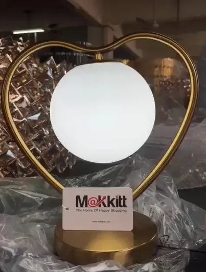 White heart shaped battery-operated LED lamp emitting a warm glow on a table.