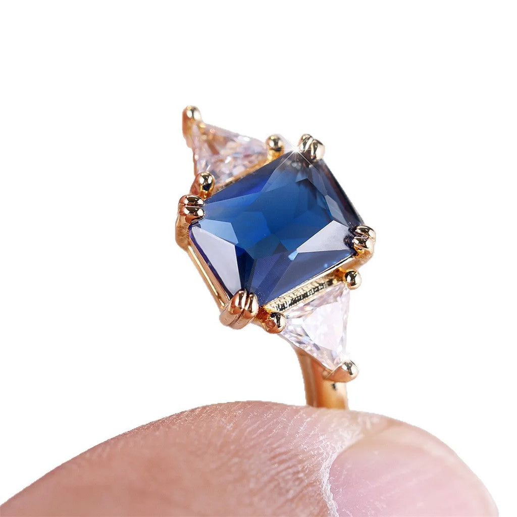 Gold and sapphire blue rectangular copper ring for women on a plain background.