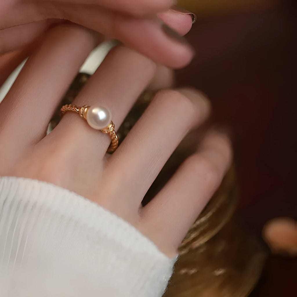 Antique finish copper ring with geometric twist and central inlaid pearl on a wooden background