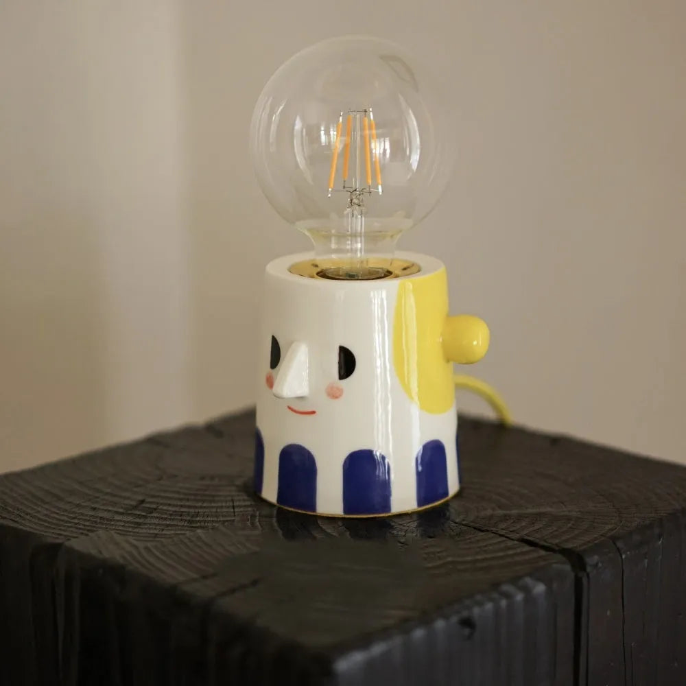 Handmade solid ceramic table lamp with spherical white shade on a wooden surface, showing UK plug.