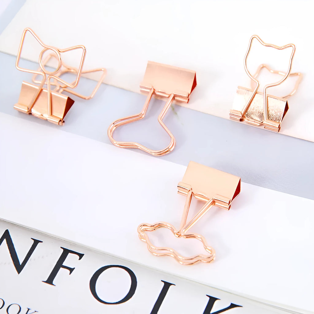 Small gold metal office clip with a long tail, shown in flamingo, love, cloud, cat, cactus, and bow shapes.