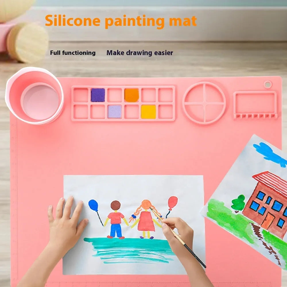Light blue silicone painting mat with two round bowls, placed on a wooden table with paint brushes