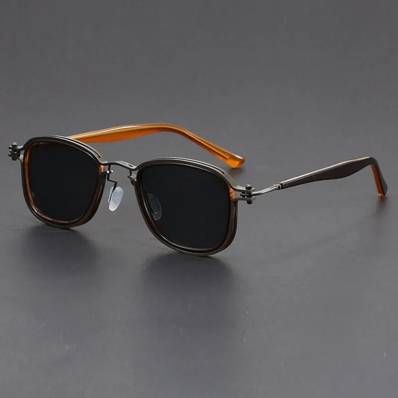 Retro square sunglasses with black gold frames and grey AC lenses on a wooden surface.