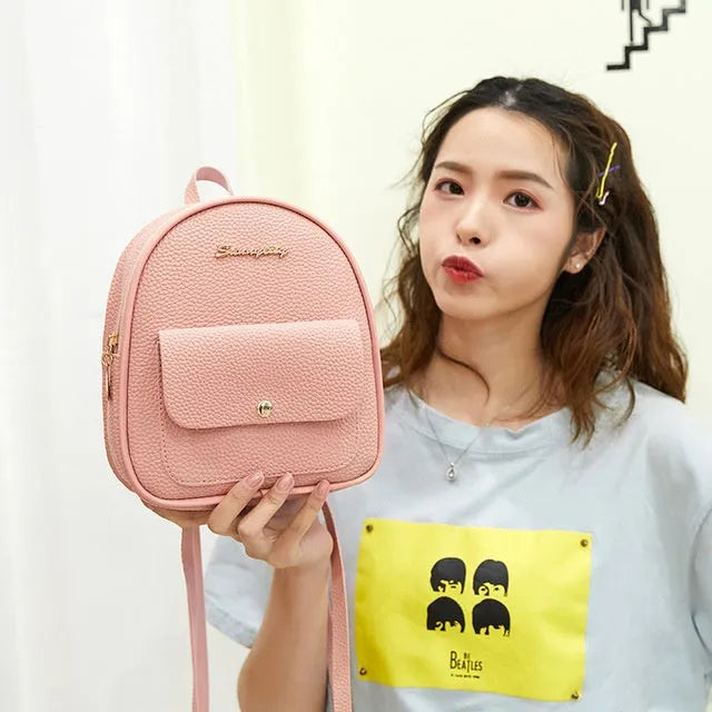 A small black PU women's shoulder backpack with a zip, shown next to a mobile phone for scale.