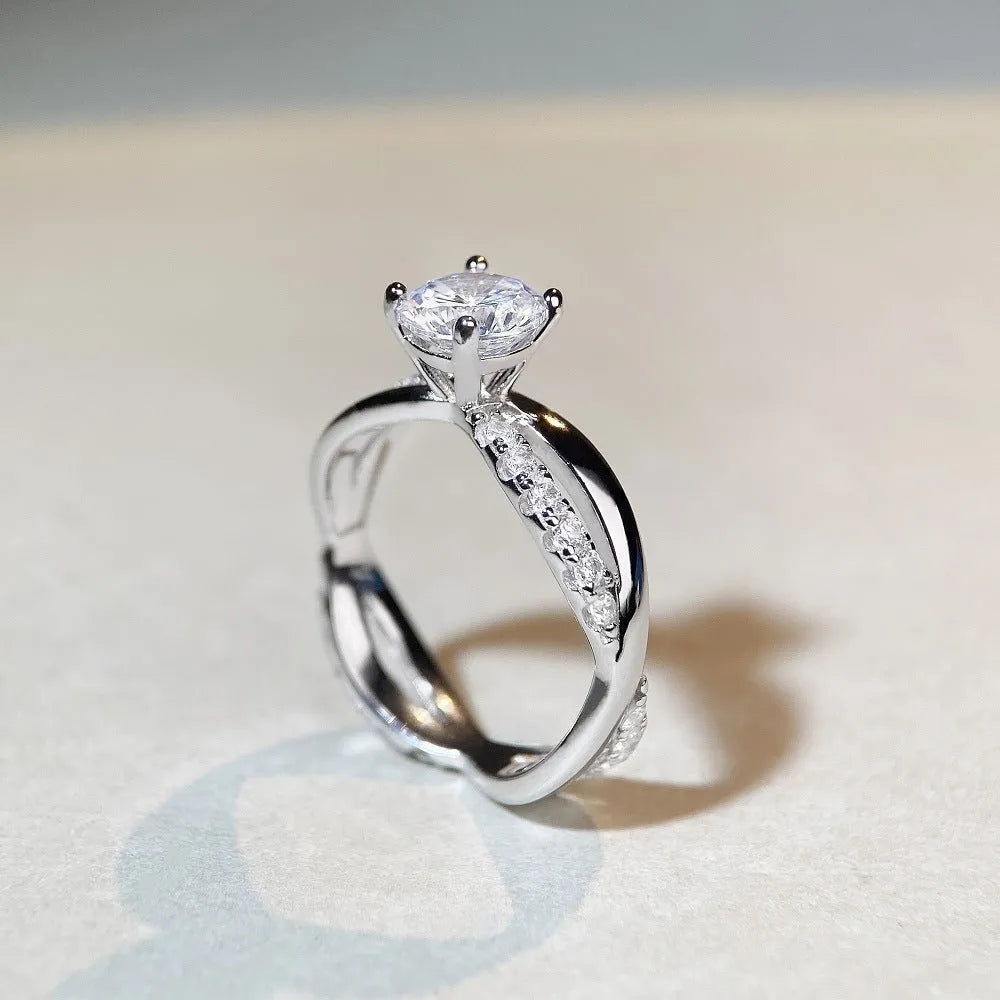 A silver ring with a 1 karat moissanite stone in a four-claw setting on a twisted geometric band.