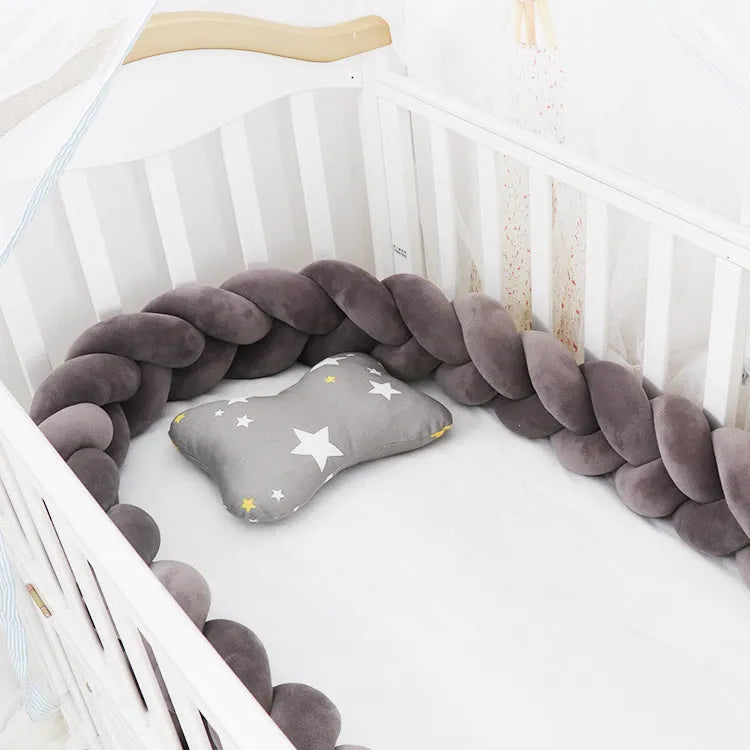 Braided knot style crib bumper in spandex velvet, wrapped around white cot rails in a nursery.