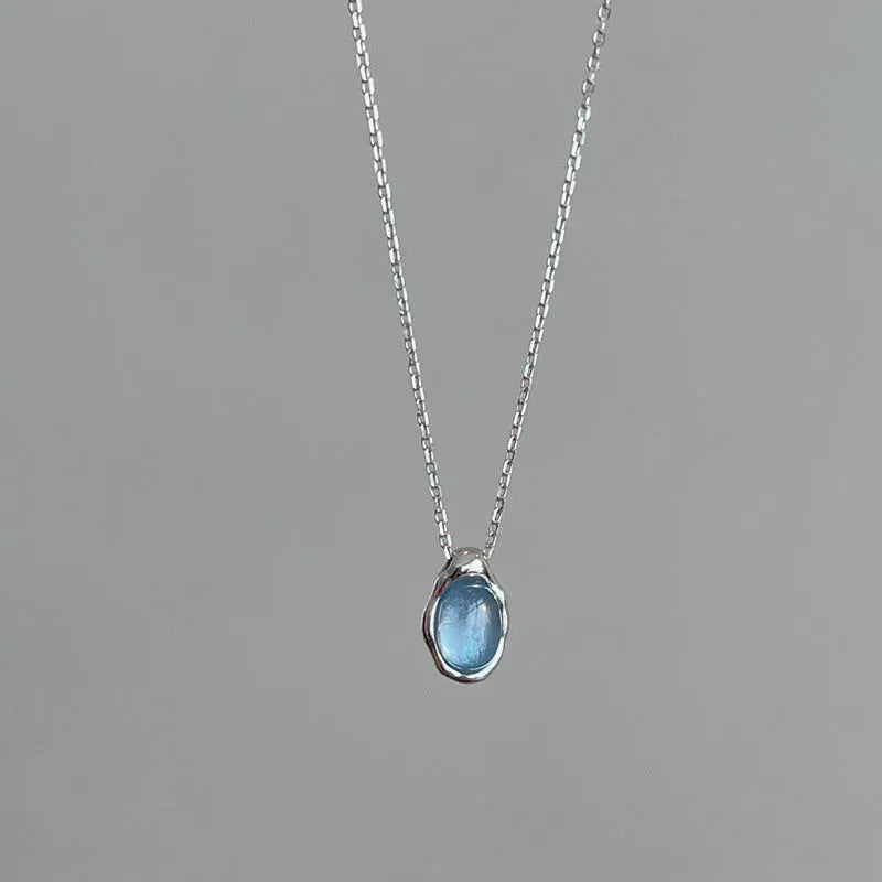 Close-up of a navy blue water drop pendant necklace with a platinum-colour finish on a textured cross chain.