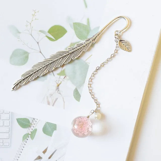 Close-up of a metal alloy bookmark with a preserved pink dried flower inside, measuring 12cm long, on an open book.