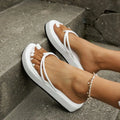 Women's white thick sole flip-flops with a herringbone rubber outsole on a sandy beach