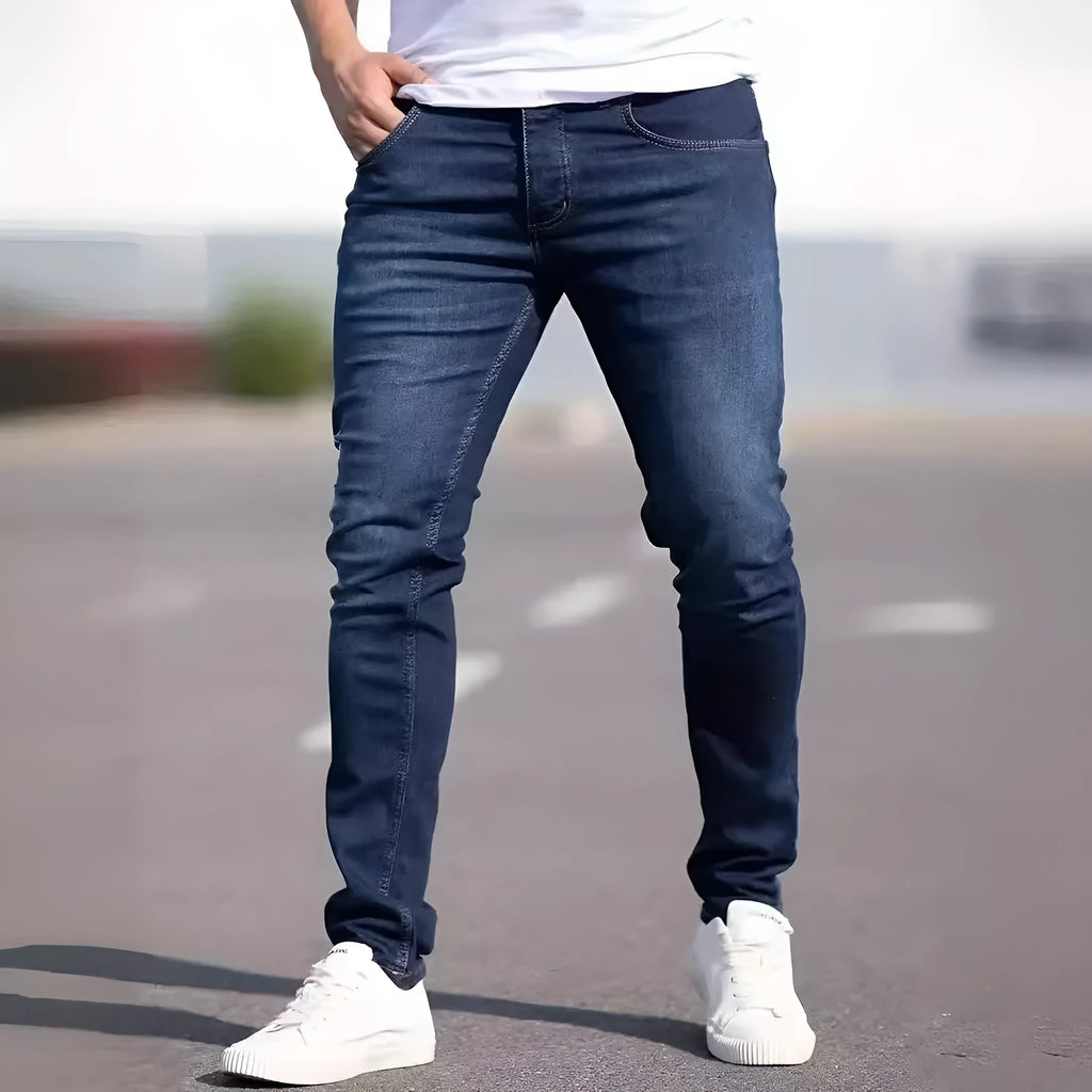 Men's dark blue slim-fit skinny jeans with a zip fly and mid-rise waist on a plain background.