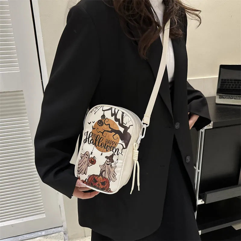 Black Halloween crossbody bag with orange pumpkin, white ghost, and black bat graffiti print, shown on adjustable strap.