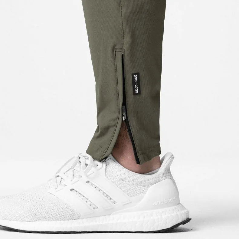 Man wearing dark grey loose-fit fitness trousers with tied ankle cuffs, made from quick-dry polyester fabric.