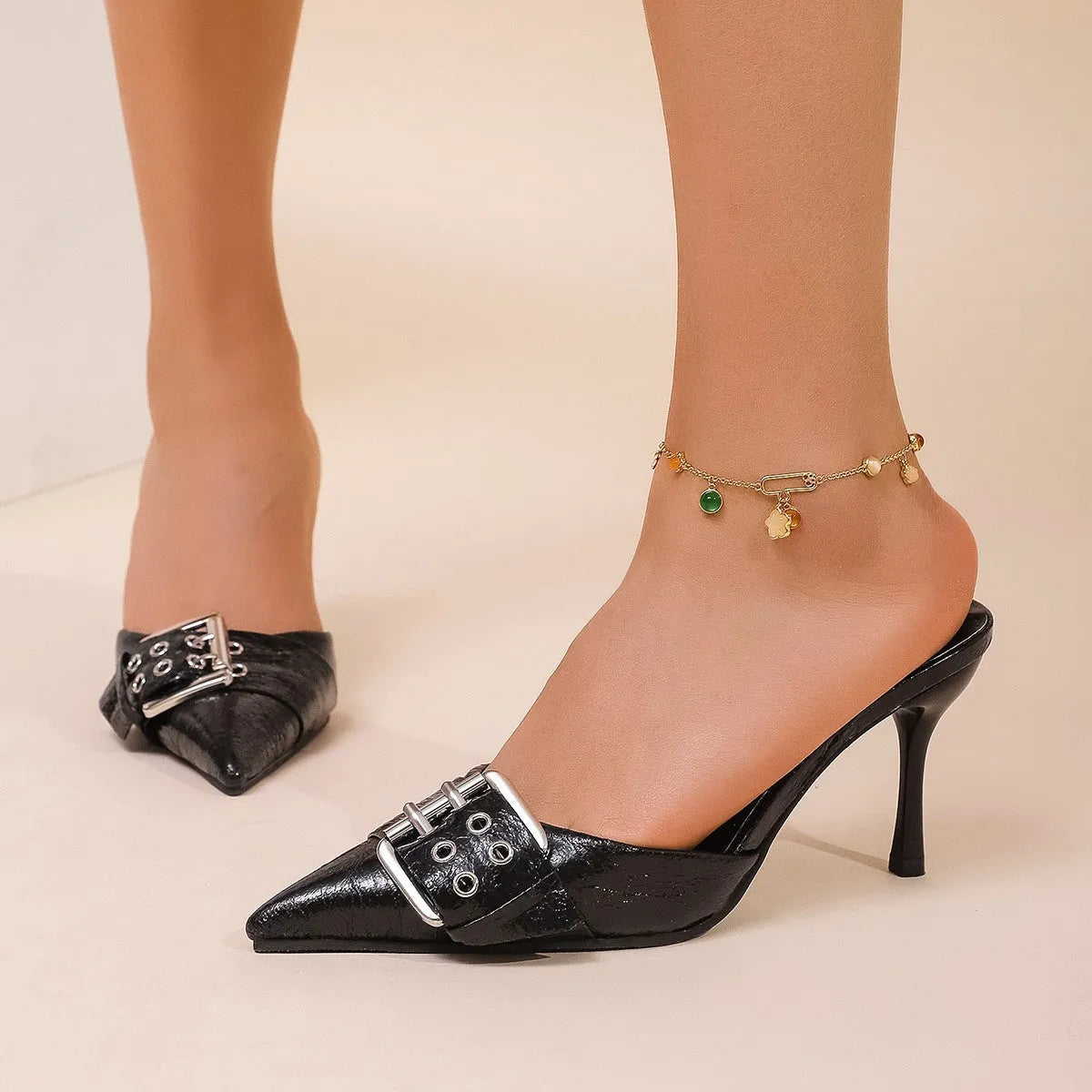 Black women's high heels with pointed toe and buckle decoration on ankle strap.