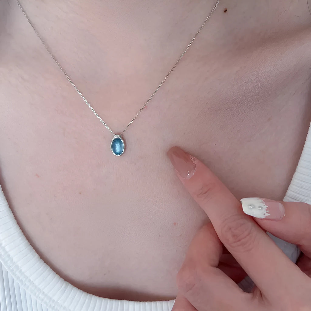 Close-up of a navy blue water drop pendant necklace with a platinum-colour finish on a textured cross chain.