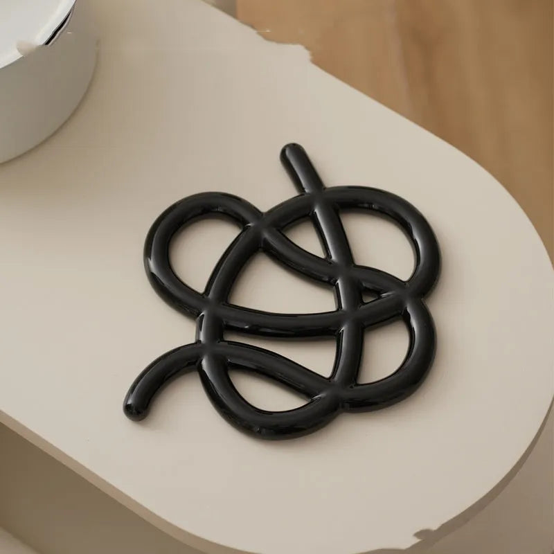 Irregular-shaped ceramic heatproof mat in a solid colour on a wooden table, protecting it from a hot pan.