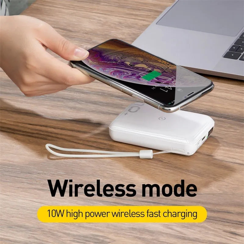 Square black wireless power bank with digital display showing battery percentage, next to a smartphone on its wireless charging surface.