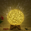 White hand-knit rattan ball lamp with USB cable and remote control on a wooden table.