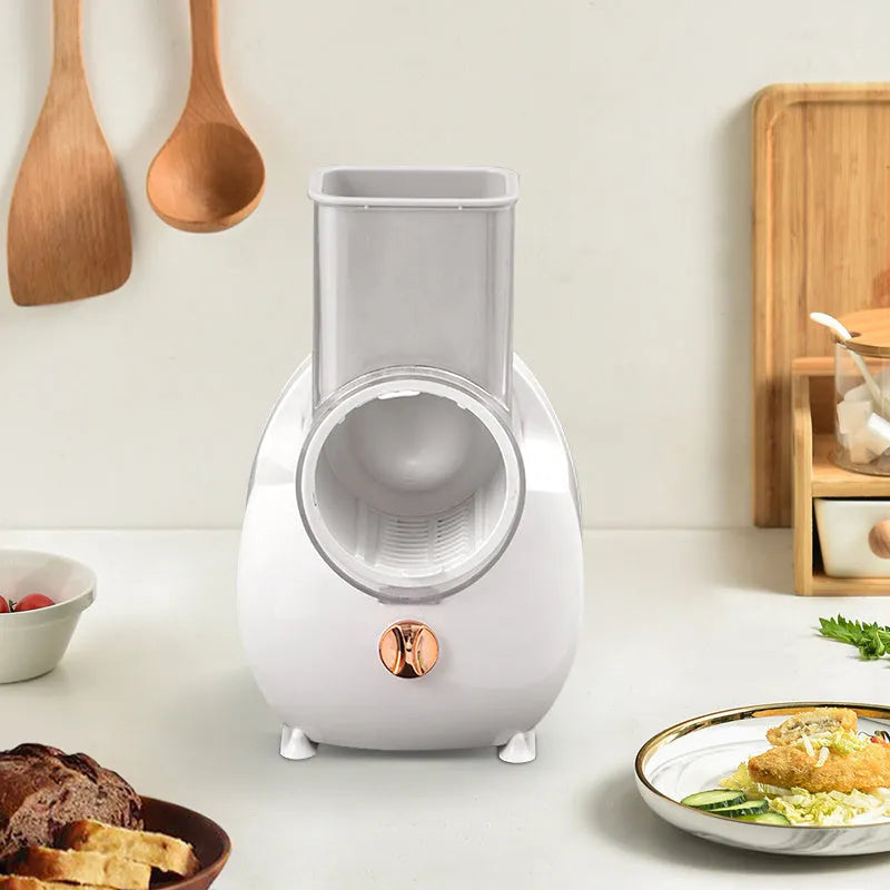 White electric vegetable slicer with rotary grater, suction base, and multiple blades on a kitchen counter.