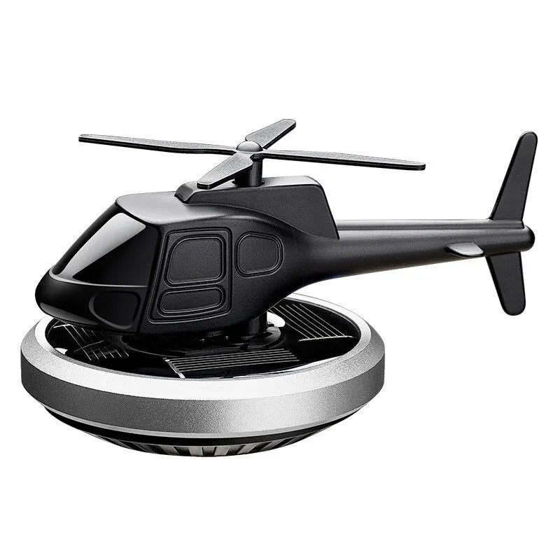 Silver metal solar-powered helicopter car air freshener clipped to a vehicle air vent, with rotating blades.