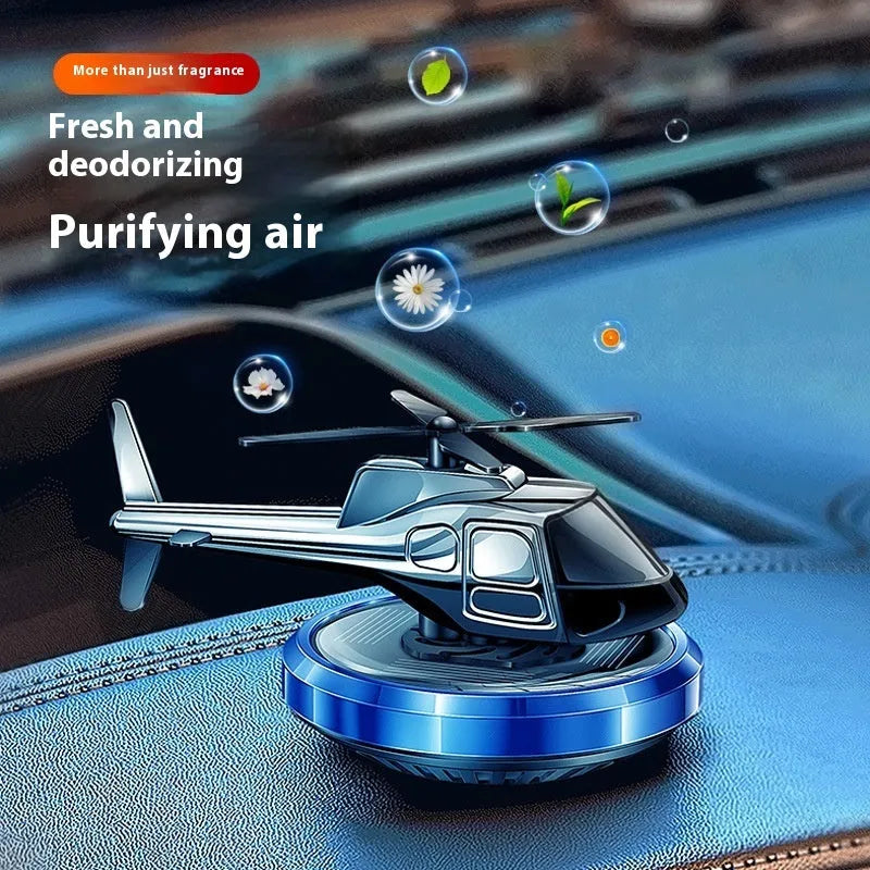 Silver metal solar-powered helicopter car air freshener clipped to a vehicle air vent, with rotating blades.