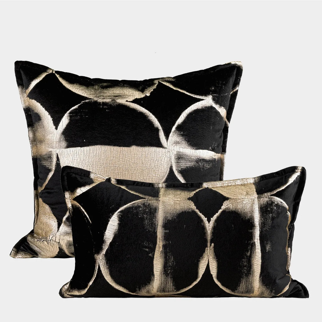 Black and gold abstract pattern decorative square and waist pillow cushions on a grey sofa.