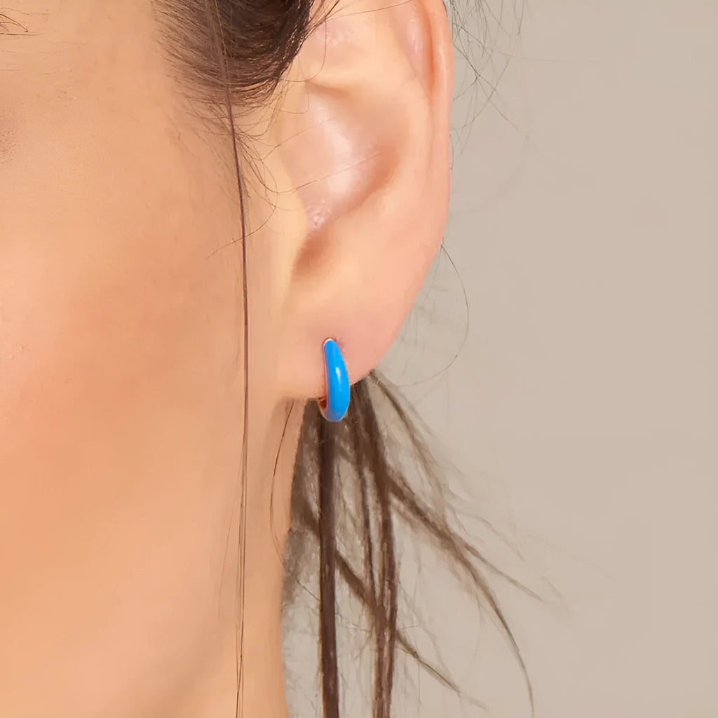A pair of curved U-shaped epoxy earrings with a translucent blue dripped oil finish and a silver hook on a white background.