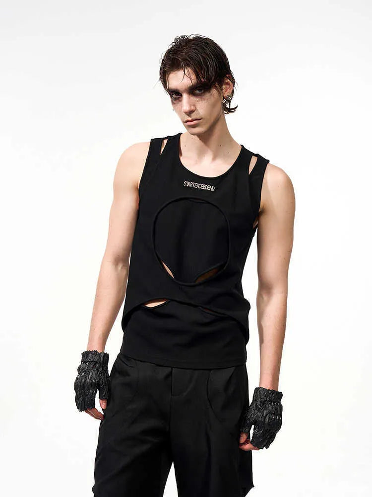 Man wearing a loose-fitting black sleeveless hollow thread waistcoat over a white t-shirt.