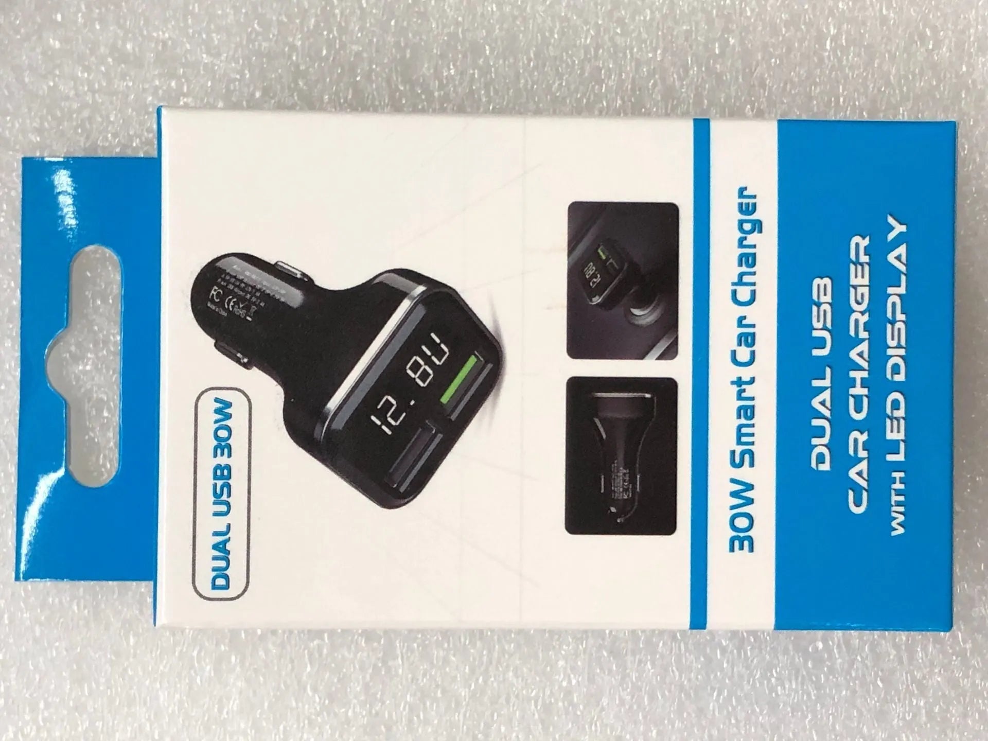 Black dual USB car charger with LCD screen displaying voltage, plugged into a car dashboard socket.