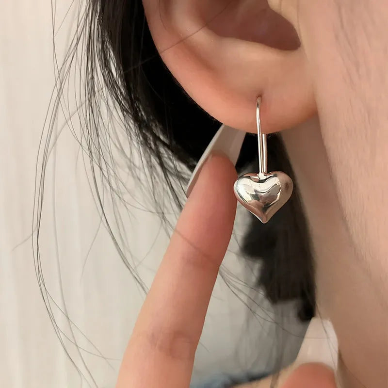 Silver glossy heart-shaped Korean-style earrings with a three-dimensional design on a white background.