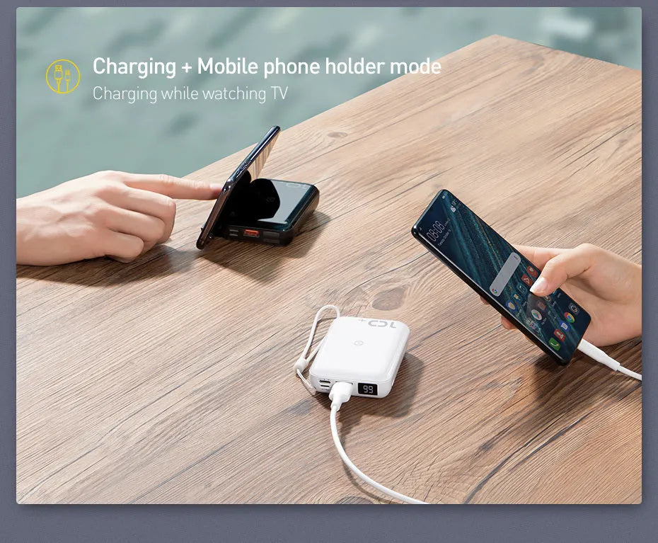 Square black wireless power bank with digital display showing battery percentage, next to a smartphone on its wireless charging surface.