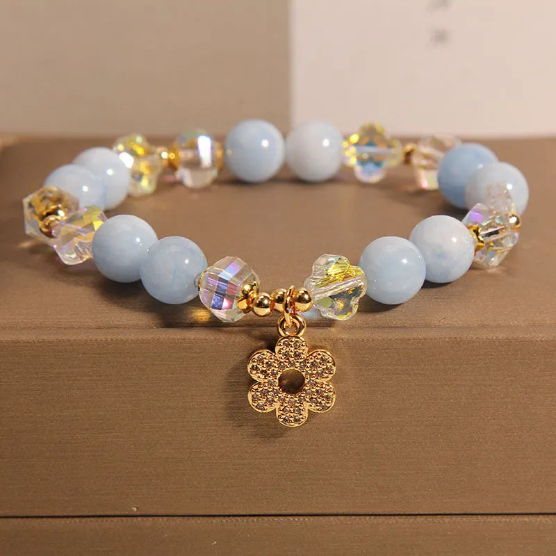 Women's aquamarine crystal bracelet with a four-leaf clover charm and pearl accent on wrist.