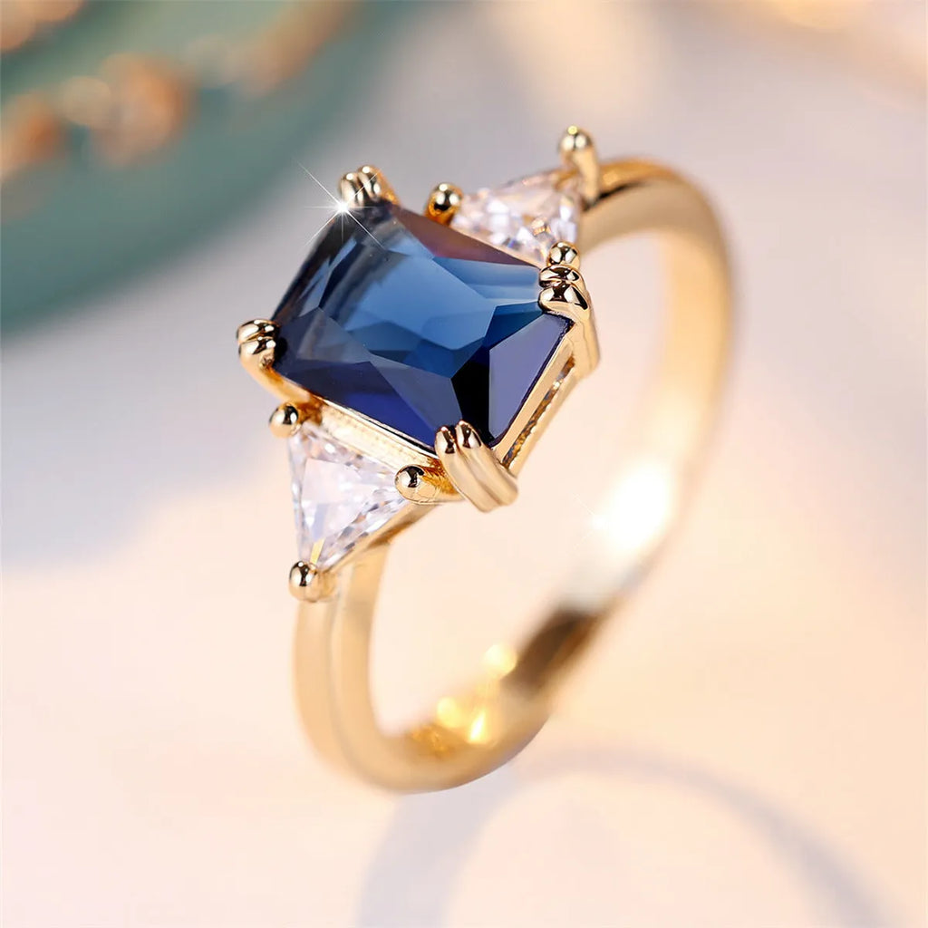 Gold and sapphire blue rectangular copper ring for women on a plain background.