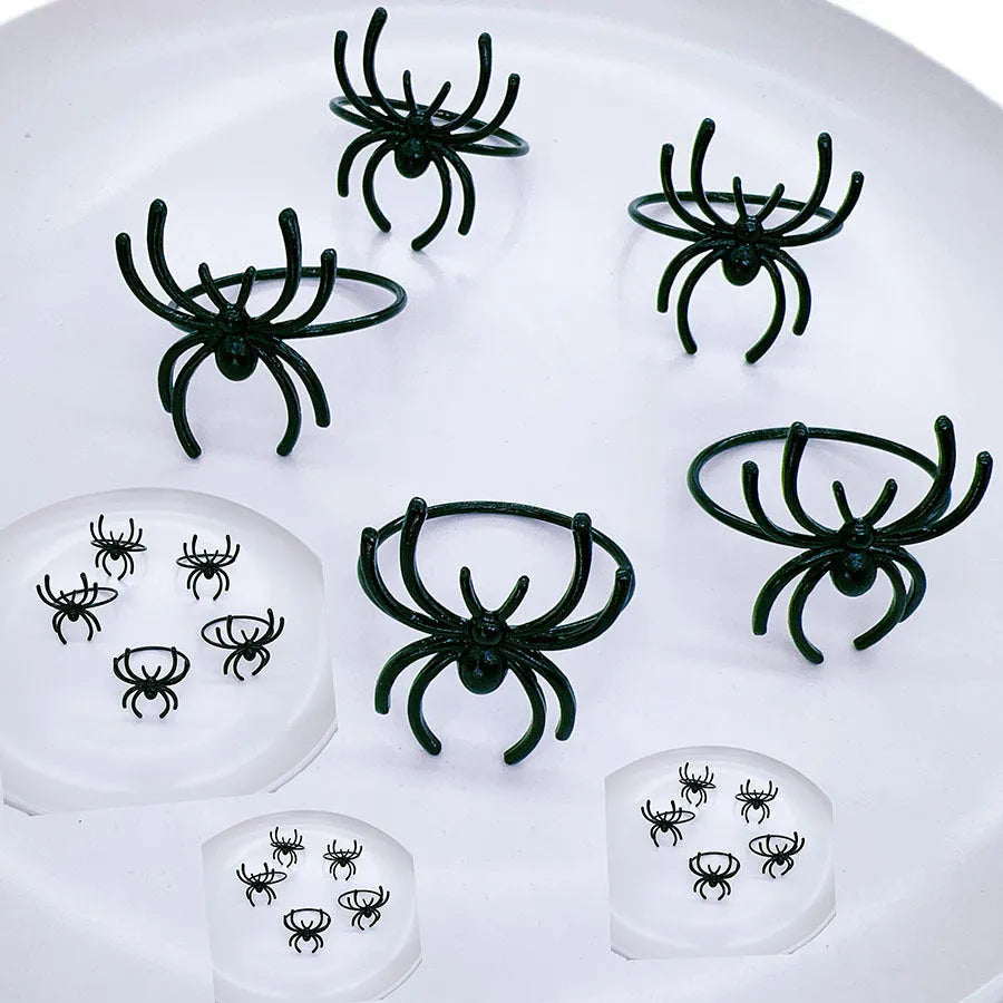 Set of six black alloy spider-shaped napkin rings on a dark tablecloth.