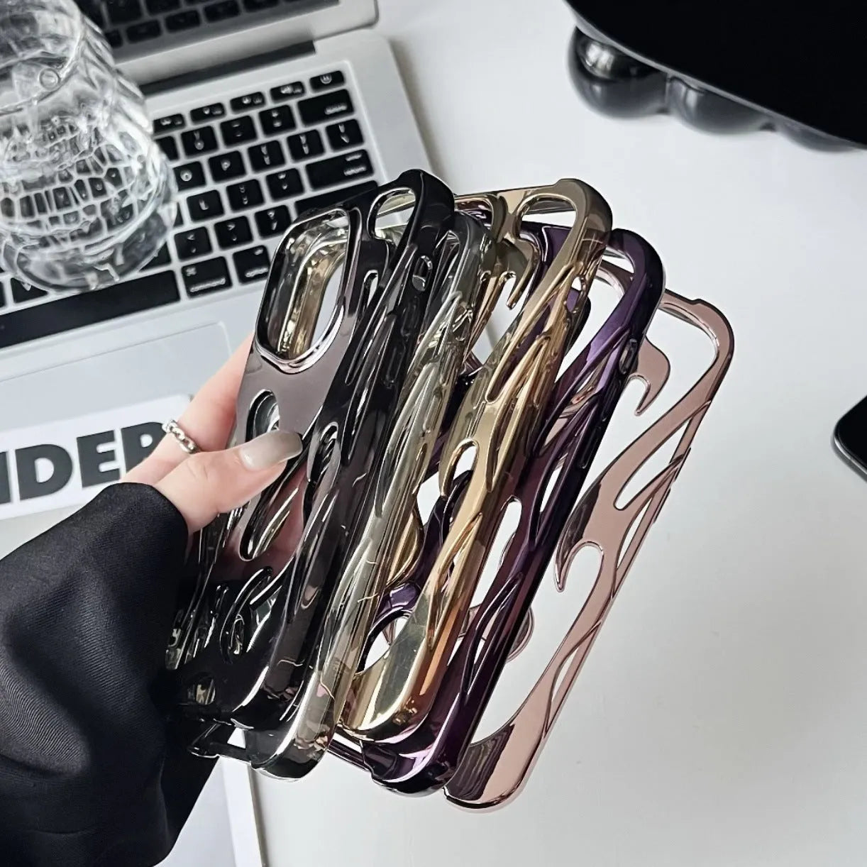 Electroplated hollow flame pattern phone case for iPhone on a table, showing silver metallic finish and cut-out design.