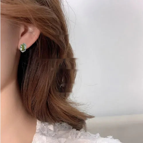 Pair of liquid olive green electroplated alloy stud earrings for women on a neutral background