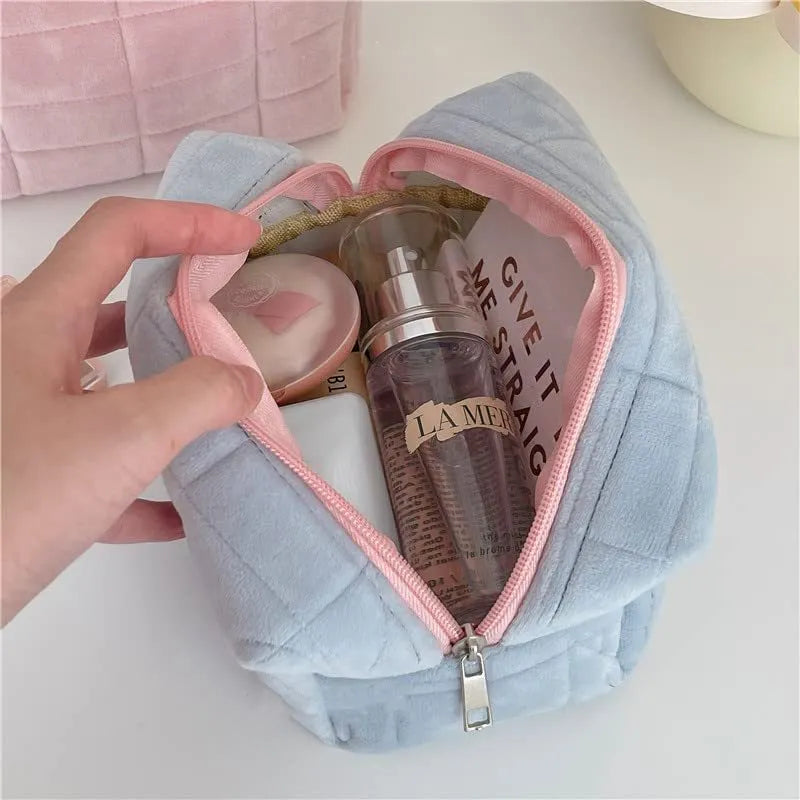 Three plush makeup bags in pink, white, and blue with zippers, laid flat showing front
