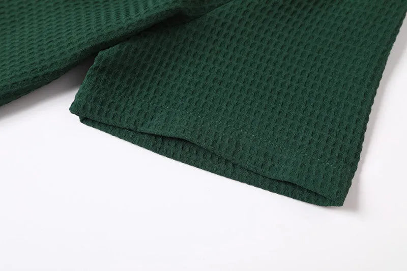 Dark green waffle patterned lapel polo shirt with short sleeves, two round metallic-texture buttons, and slightly arc-shaped hem.